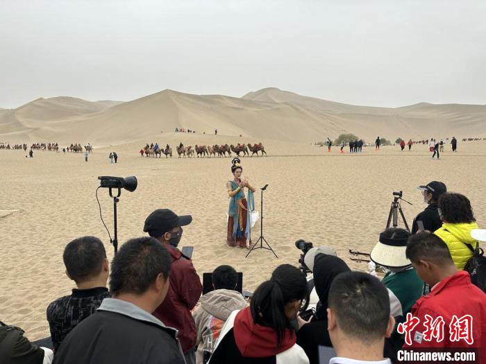 圖為2023年4月底，敦煌大漠“逐舞者”奧楠在鳴沙山月牙泉景區視頻直播，吸引游人圍觀。　馮志軍 攝